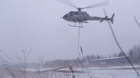 Helikopteri nostaa harmaassa talvisäässä sähkötolppaa maasta ilmaan.