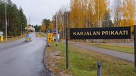 A sign that reads "Karelia Brigade" in Finnish, posted by a road lined with golden-coloured trees in the autumn.