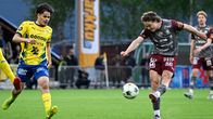 n spelare i grått sparkar en fotboll medan en spelare i gult springer intill.