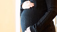 Bild på gravid mage. Kvinnan bär en svart stickad klänning och vilar händerna på magen.