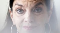 Anna-Leena Härkönen katsoo kameraan , vaalea hunnuke tulee Anna-Leenan kasvojen puoleenväliin etualalla olevista kuivakukista.
