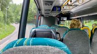 Passagerare sitter på en buss, vägen och grönska syns ute.