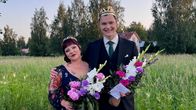 Hanna Hirvonen ja Veeti Tikkanen seisovat vierekkäin ulkona ja hymyilevät. Molemmilla on päässään kruunu ja käsissään kukkia.