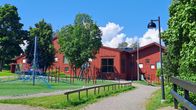 En röd träbyggnad som är Kyrkfjärdens skola i Ingå. Lekplats utanför skolan.