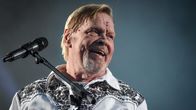 Vesa-Matti Loiri istuu juhlakonsertissaan lavalla ja nauraa katsoen yleisön suuntaan.