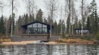 Moderni huvila metsän reunassa järven rannalla. Rakennuksessa on suuri terassi ja laituri etualalla.