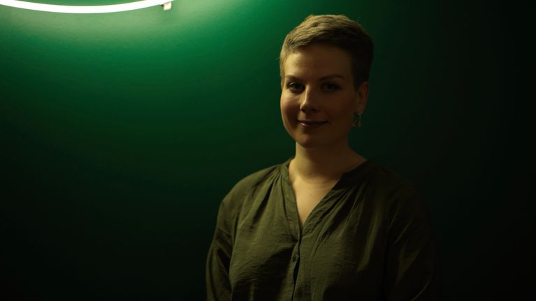 Jenni Pitko katsoo hymyillen kameraan vihreän seinän edessä. 