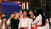 Daniela Owusu, Finlands lucia 2024, med luciaklädsel och ljus i sitt hår och Alma Pöysti och luciakören bakom i Helsingfors domkyrka.