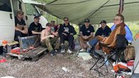 Hard core -festivaaleille tulleet nuoret miehet istuvat pressukatoksen alla. Maassa näkyy pulloja ja tyhjä makkarapaketti.