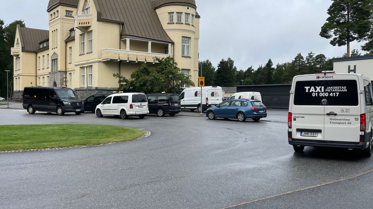 Flera vita och svarta taxibilar står parkerade utanför en större gul byggnad.