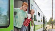 Kaksi lapsinäyttelijää seisoo kaulakkain kiskobussin oviaukossa ja katsoo kameraan.