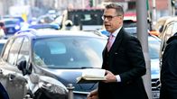 Alexander Stubb kävelee muistivihko kädessään kadulla, puku päällä, autojen ohi.