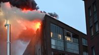 Pelastuslaitoksen nosturin kori, jossa pelastajat työskentelevät, peittyy savuun palavan kerrostalon katon korkeudessa.
