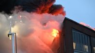 Pelastuslaitoksen nosturin kori, jossa pelastajat työskentelevät, peittyy osittain savuun palavan kerrostalon katon korkeudessa.