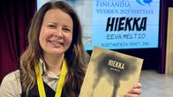 Hymyilevä Eeva Meltio pitää kädessään sarjakuva-albumia, jonka kannessa lukee Hiekka.