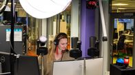 Kuvassa henkilö työskentelee radiostudiossa. Hänellä on kuulokkeet päässään ja hän käyttää miksauspöytää sekä tietokonetta lähetyksen ohjaamiseen. 
