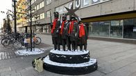 Pronssinen tiernapoikapatsas Oulun keskustassa. Tiernapohilla on oranssit kaulahuivit kaulassa. 
