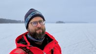 Talvivaatteisiin pukeutunut mies katsoo kameraan järven jäällä.