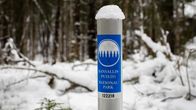 Kansallispuisto-merkki lumisessa metsässä olevassa metallisessa tolpassa.
