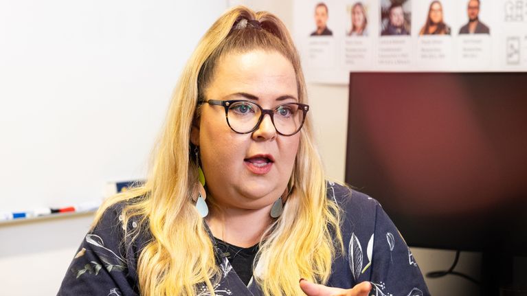 Paula Silven istuu työtuolissa ja selittää käsillään haastattelussa valkoseinäisessä toimistohuoneessa. 