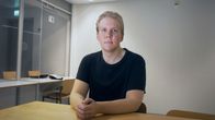 Nuori valkoinen mies istuu pöydän ääressä ja katsoo kameraan.