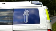Lähikuvassa on valkoisen pakettiauton perä, jossa on sininen tarra ja siinä logo.