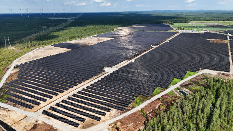 Aurinkovoimala jossa tuhansia aurinkopaneeleita. Taustalla näkyy myös tuulivoimaloita.