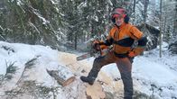 En man med skyddskläder står i en snötäckt skog med en motorsåg.
