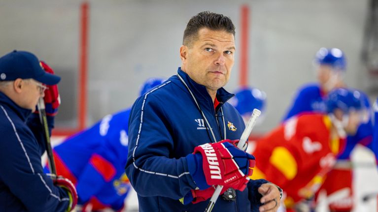 Tomek Valtonen seisoo kaukalossa maila kädessään, taustalla joukko pelaajia harjoittelee.