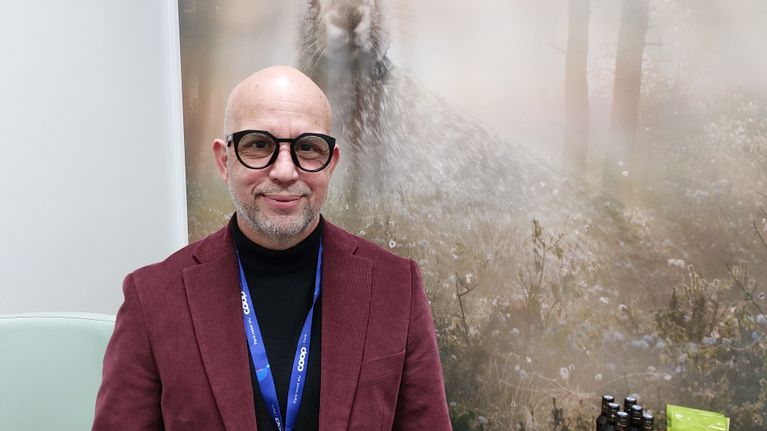 Antonio Boadas med röd kavaj framför en naturbild med en hare.