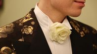 Yksityiskohta Linnan juhlien puvusta: valkoinen ruusu miehen kauluksessa.