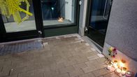 Kynttilöitä ja kukkia on asetettu kerrostalon rappukäytävän ulkopuolelle. Ulko-ovessa on keltaista teippiä.