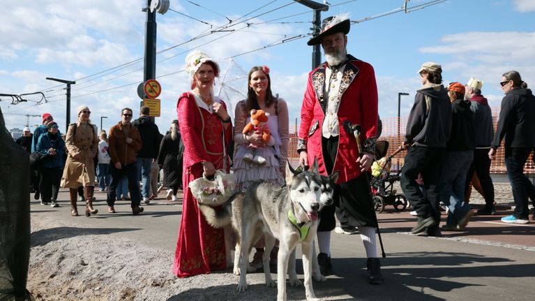 Kolme vanhan ajan tyyliin pukeutunutta henkilöä ja kaksi koiraa.