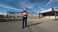 Škoda Transtech Otanmäen tehtaan pääluottamusmies Mikko Komulainen oranssi-mustassa työvaatteessa seisoo tehdasalueen portin edessä, taustalla tehdas.