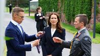 Kolme henkilöä seisoo ulkona, yksi henkilöistä pitelee kädessään kravattia.