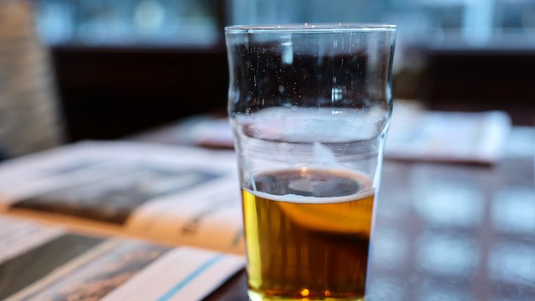 Photo shows a pint of lager on a table.