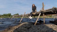 Nainen istuu puurakenteisella lippoussillalla Tornionjoen Kukkolankoskella.