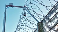 Looking up at coils of barbed wire atop a metal fence with a light and/or sensor above.