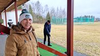 Pipopäinen nainen ja kaksi taustalla harjoittelevaa miesgolfaajaa harjoitusradalla 