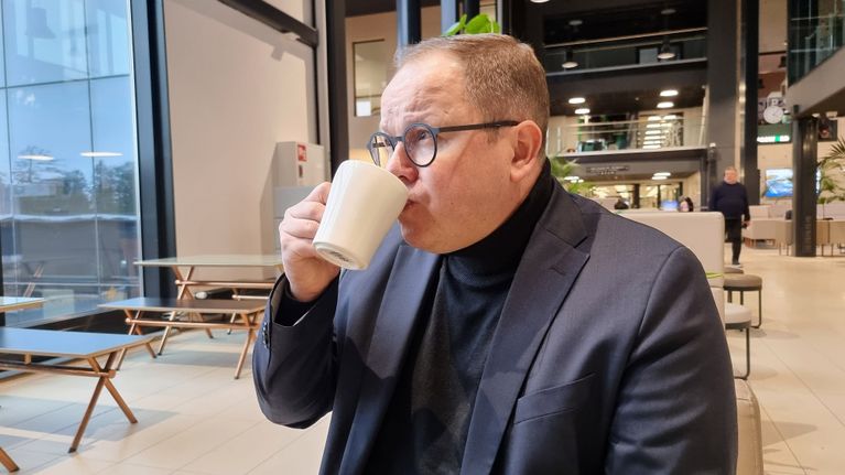 Rehtori Juha-Matti Saksa rentoutumassa kahvikupin ääressä modernissa kahvilaympäristössä.