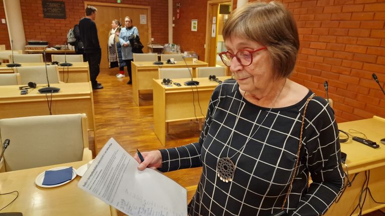 nainen katsoo paperia jossa näkyy tekstiä.