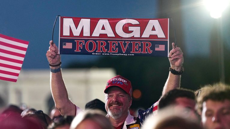 Hymyilevä ihminen pitää käsissään Maga Forever viiriä.