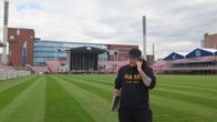 Kalle Kallonen puhuu puhelimeen nurmikentällä. Taustalla näkyy katsomoita.
