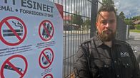 En säkerhetsvakt står bredvid en skylt som listar förbjudna föremål.