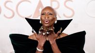 Cynthia Erivo puhaltaa lentosuukon. Erivo on kalju, näyttävät korvakorut, sormukset ja kynnet. Yllään tumman vihreä samettinen iltapuku, jossa pystyssä oleva kaulus.