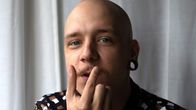 Lähikuvassa Aleksin kasvot, kun hän haroo sormillaan viiksiään. Hän on kolmekymppinen mies, jolla on siilitukka ja korvavenytys.
