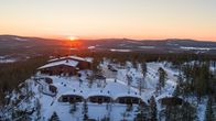 Talviseen vaaramaisemaan rakennettu majoitusliike mökkikylineen, taustalla auringonlasku.
