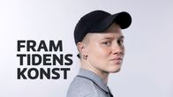 Närbild på Edith Hammar i en svart keps, hon ser in i kameran, bakom hennes syns en textplansch där det står framtidens konst.