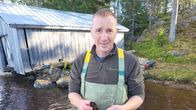 En man i vadarstövlar som står i vattenbrynet intill stranden. 