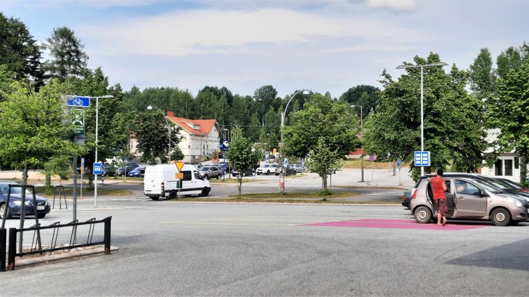 Autoja parikkipaikalla. Taustalla vaalei puurakennus, joka on Parikkalan rautatieasema. 